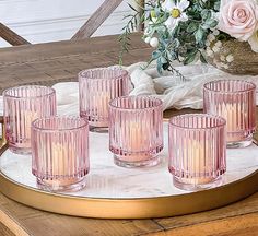 six pink glass tumblers on a tray with flowers in the backgrounnd