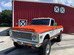 an orange and white truck parked in front of a red barn