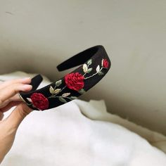 a hand holding a black headband with red roses on it