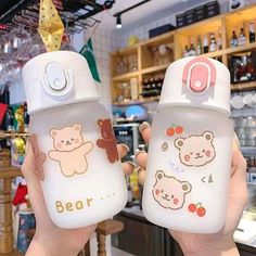 someone holding up two baby bottles with bear designs on them in front of a store