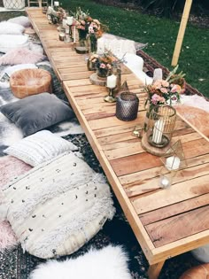 a long wooden table sitting on top of a lush green field covered in lots of pillows