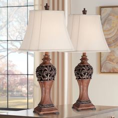 two lamps sitting on top of a wooden table next to a window with curtains in the background