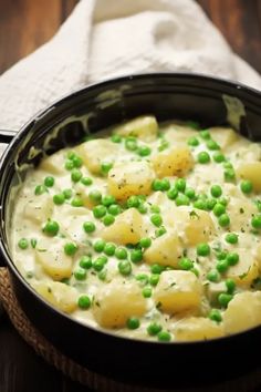 a pot filled with potatoes and peas on top of a wooden table