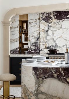 an elegant kitchen with marble counter tops and black cabinets, along with a bar stool