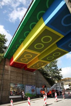 the underside of a multicolored building with people walking underneath it and trees in the background