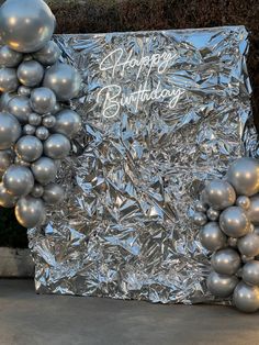 a bunch of silver balloons sitting on top of a piece of tin foil with the words happy birthday written on it