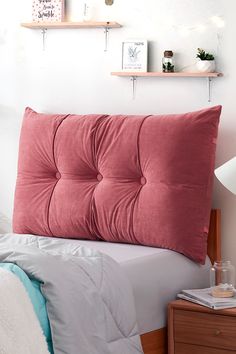 a bed with pink and white pillows in a bedroom next to a shelf filled with books