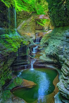 a small waterfall in the middle of a forest with green moss growing on it's sides