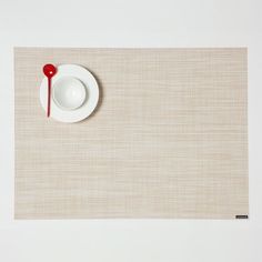 a place mat with a white plate and red spoon sitting on it next to a cup