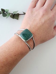 This large square Larsonite* is a deep sea-green color with darker greens sweeping across its surface. Simply set atop a cuff bracelet, the curving lines of silver give this statement cuff an elegant, feminine style. On the underside of the stone, waves of silver are cut away to reveal the beautiful underside of this unique stone. Heavy gauge silver triangle wire is curved and rounded to give this cuff a comfortable fit. Made in fine and sterling silver, the bracelet has been oxidized and given Modern Green Malachite Jewelry, Modern Green Cuff Bangle Bracelet, Modern Green Gemstone Bracelets, Modern Green Bangle Jewelry, Modern Green Cuff Bracelet As Gift, Modern Green Cuff Bracelet Gift, Modern Green Cuff Bracelet For Gift, Modern Green Bangle, Handmade Green Cuff Bracelet For Formal Occasions