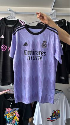 a person holding up a purple shirt in front of other soccer shirts