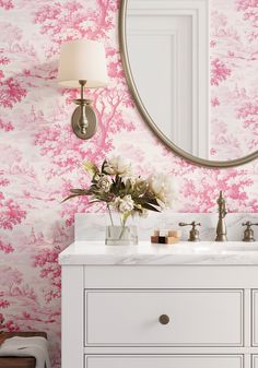 a bathroom with pink and white wallpaper and a round mirror on the wall above it