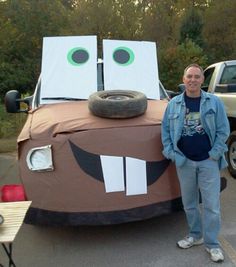 a man standing next to a fake car made out of cardboard boxes with googly eyes