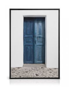 an open blue door in front of a white wall with sand on the ground below