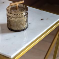 a small glass jar sitting on top of a white marble table next to a gold colored chair