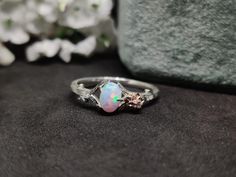 a white opal ring sitting on top of a black surface next to flowers and a gray blanket