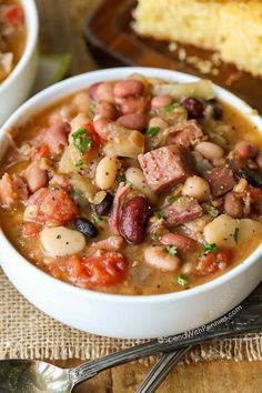 two white bowls filled with bean and sausage soup next to a slice of bread on the side