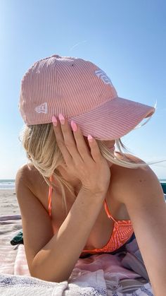 a woman laying on top of a beach next to the ocean wearing a pink hat