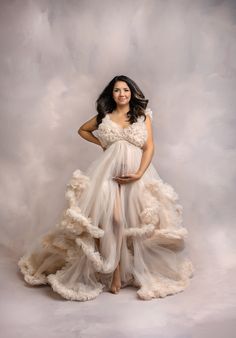 a pregnant woman in a white gown posing for a photo with her hands on her hips