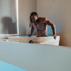 a man with dreadlocks standing on top of a bathtub in a bathroom