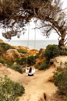 a woman sitting on a swing in the sand