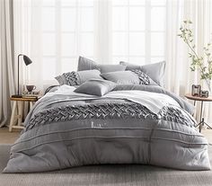 a bed with grey and white comforters in a room next to a window,