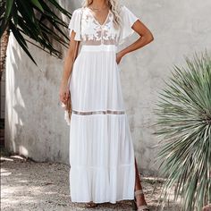 a woman wearing a white dress and sandals standing in front of a wall with palm trees