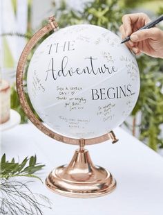 a person is writing on the globe that says the adventure begins and there are plants in the background