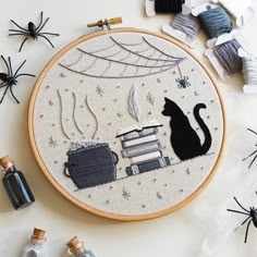 an embroidery project with cats, books and spider webs on the table next to it