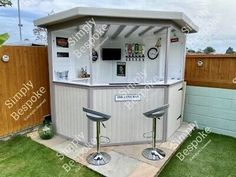 an outdoor bar with two stools in the grass next to a fence and wooden fence