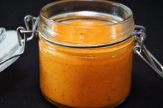 a glass jar filled with orange colored liquid on top of a table next to a spoon