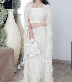 a woman in a white dress with a large feather cape on her head and holding a bouquet