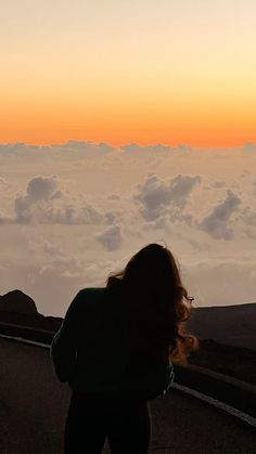 a woman standing on the side of a road with clouds in the background