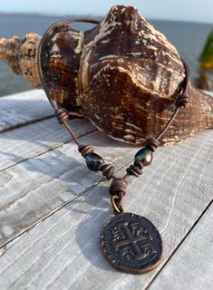 An antiqued oxidized look coin replica of Spanish dollars. These were created by the Spanish as currency to trade for things they needed. Pirates also took over the vessels and many of the coins (also called "Spanish dollars" and "pieces of eight") have been found on those shipwrecks.  This replica coin has become a trendy surfer style of necklace. The pendant has been attached to a, antiqued barnwood  2mm leather. It is adorned by stunning iridescent freshwater peacock pearls. The pearls are baroque which means they are off round and irregular. One of the pearls has a dimple in that adds to the uniqueness and individuality of each pearl. The pearls are secured by hand knotted barrel knots.  The leather has some distressing.  It is anticipated the leather will  distress as you wear it whic Pirate Necklace, Pieces Of Eight, Peacock Pearls, Surfer Style, Leather Pieces, Barnwood, Charm Necklace, Hand Knotted, Barrel