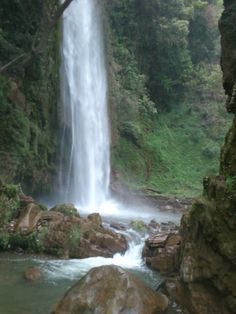 a large waterfall in the middle of a forest filled with rocks and water flowing down it's sides