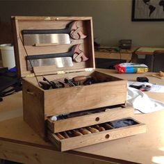 an open wooden box on top of a table filled with crafting supplies and tools