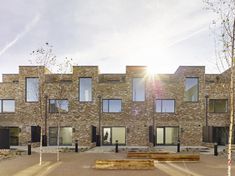 an empty park bench in front of a brick building with lots of windows and doors