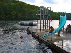 people are swimming in the water near a dock with a slide and pool toys on it