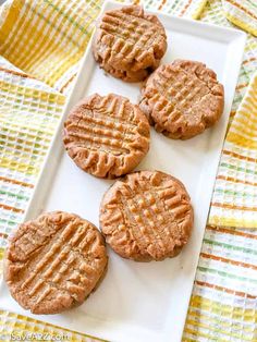 four peanut butter cookies on a white plate with a yellow and green napkin behind them