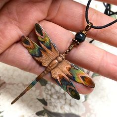 a hand holding a necklace with a dragonfly on it