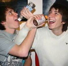 two young men are drinking from bottles together