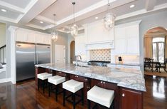 a large kitchen with marble counter tops and wooden flooring, along with white cabinetry