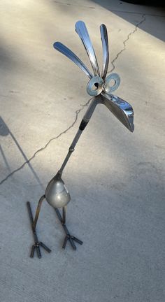 a metal sculpture of a bird holding an umbrella on its back legs with one foot