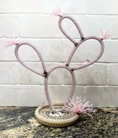 a small plant with pink flowers in a basket on a table next to a brick wall