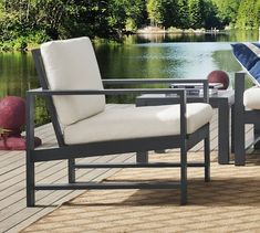 two chairs sitting on top of a wooden deck next to a body of water with trees in the background