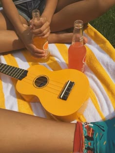 an orange ukulele sitting on top of a towel next to two bottles of soda