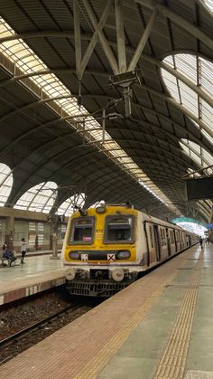 a yellow and white train pulling into a station with people walking on the platform next to it