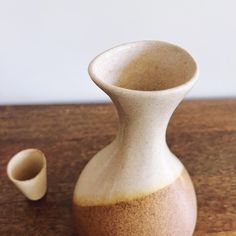 a white and brown vase sitting on top of a wooden table next to a cup