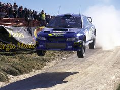 a blue car jumping over a dirt road in front of a crowd