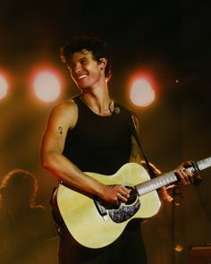 a man holding a guitar in his right hand and singing into a microphone on stage